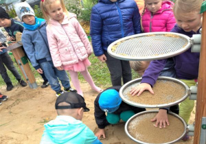dzieci sypią i obserwują piasek na sitach w ogrodzie na terenie ogródka "Słoneczna Akademia"